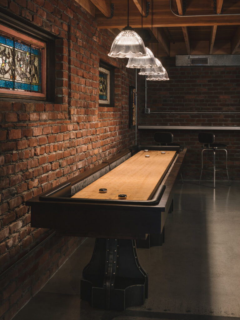 Shuffleboard table running along the exposed brick wall on polished concrete.