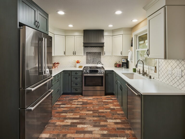 The kitchen from the dining side, with green beadboard lower cabinets, quartz counters, and a brick-look tile floor.