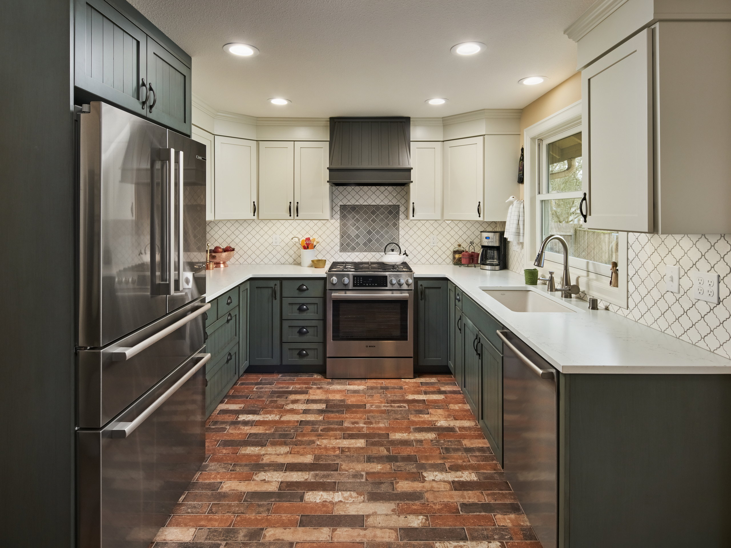 The kitchen from the dining side, with green beadboard lower cabinets, quartz counters, and a brick-look tile floor.