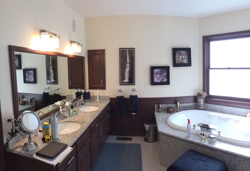 The bathroom before remodeling, with a cherry double vanity, granite counters, beadboard wainscot, and a corner jetted tub.