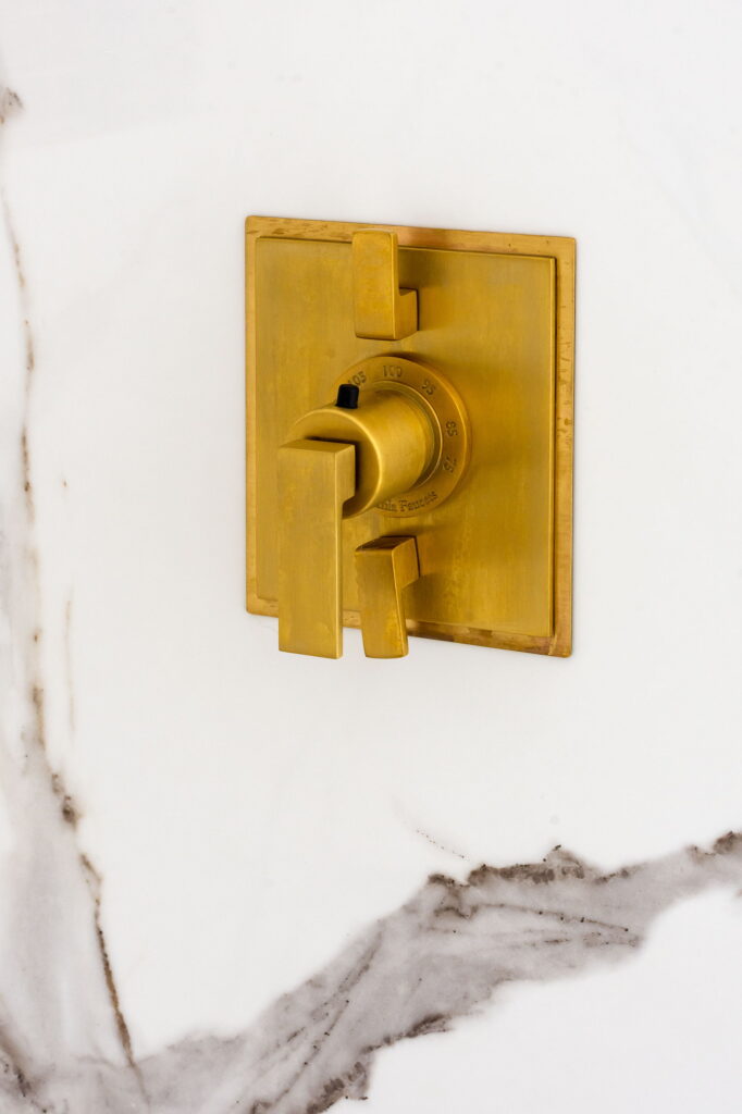 Brass thermostatic shower valve with a temperature dial, mounted on the marble slab wall.
