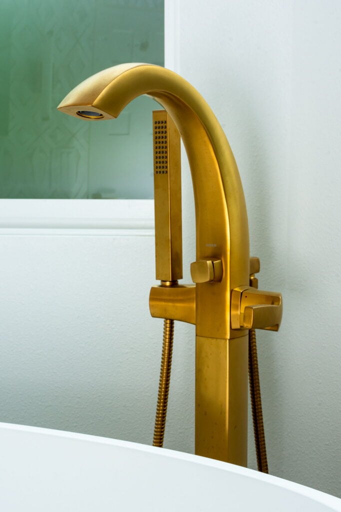 Brass floor-mount tub filler with a handheld sprayer, beside the freestanding tub.