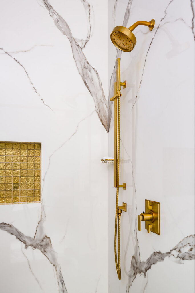 Brass shower fittings and a gold glass mosaic niche against book-matched marble slab.