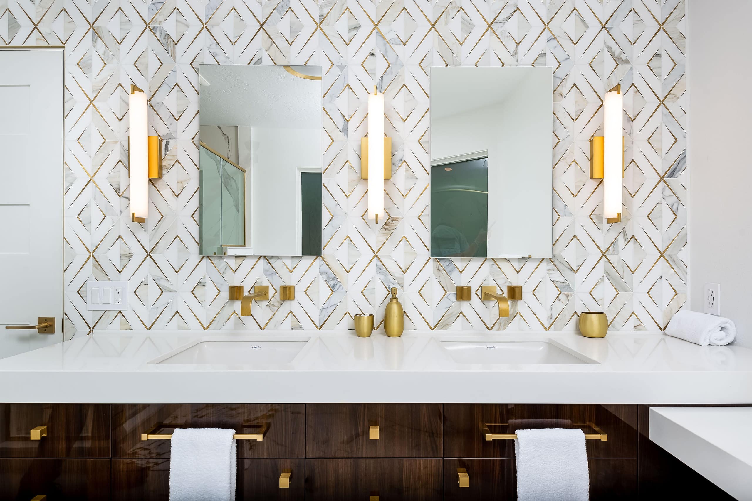 Double vanity seen head-on, with wall-mounted brass faucets and paired mirrors on the inlay tile.
