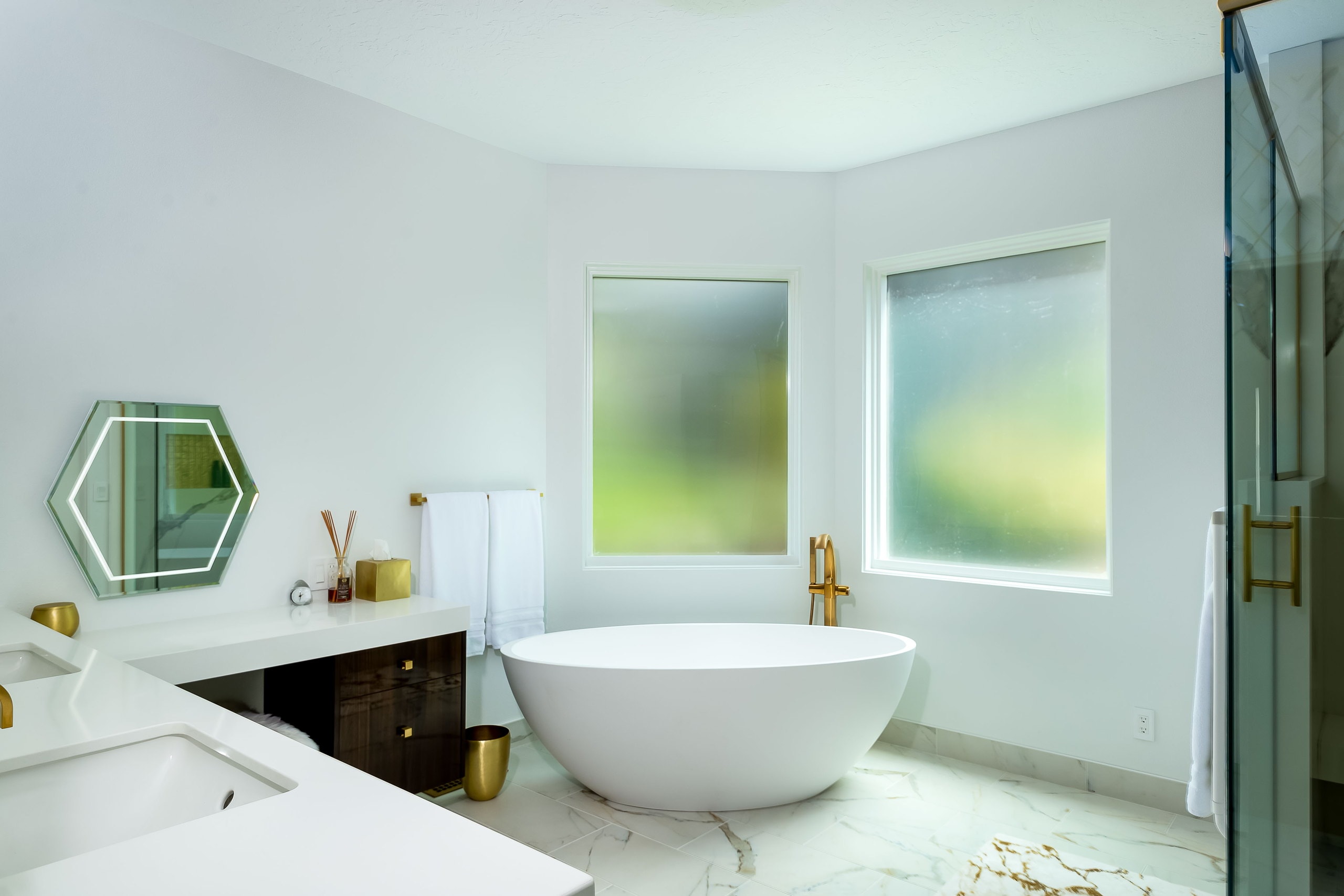 Freestanding oval soaking tub set in a corner between two obscured-glass windows.