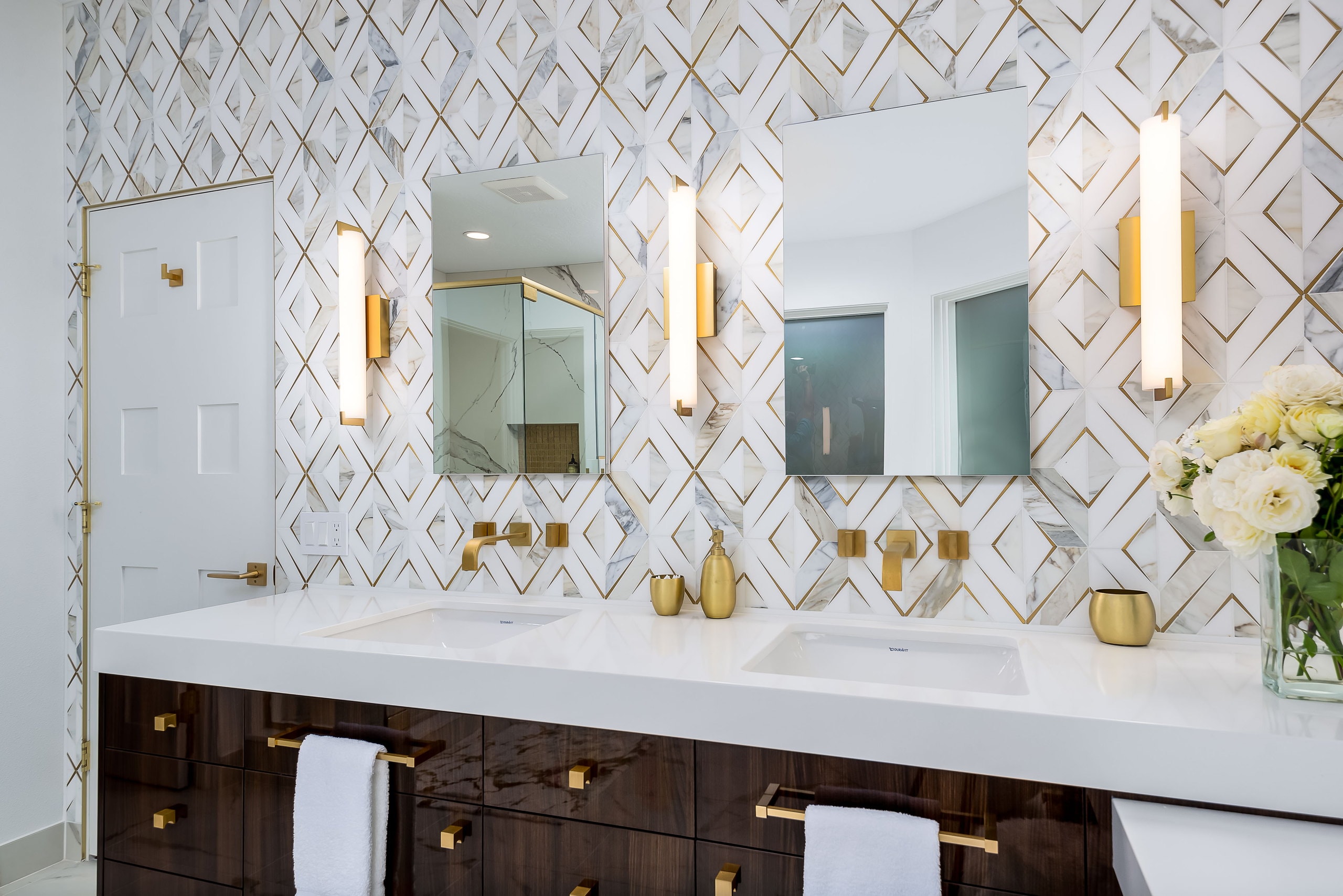 The vanity run from the doorway, with brass sconces set between the mirrors.