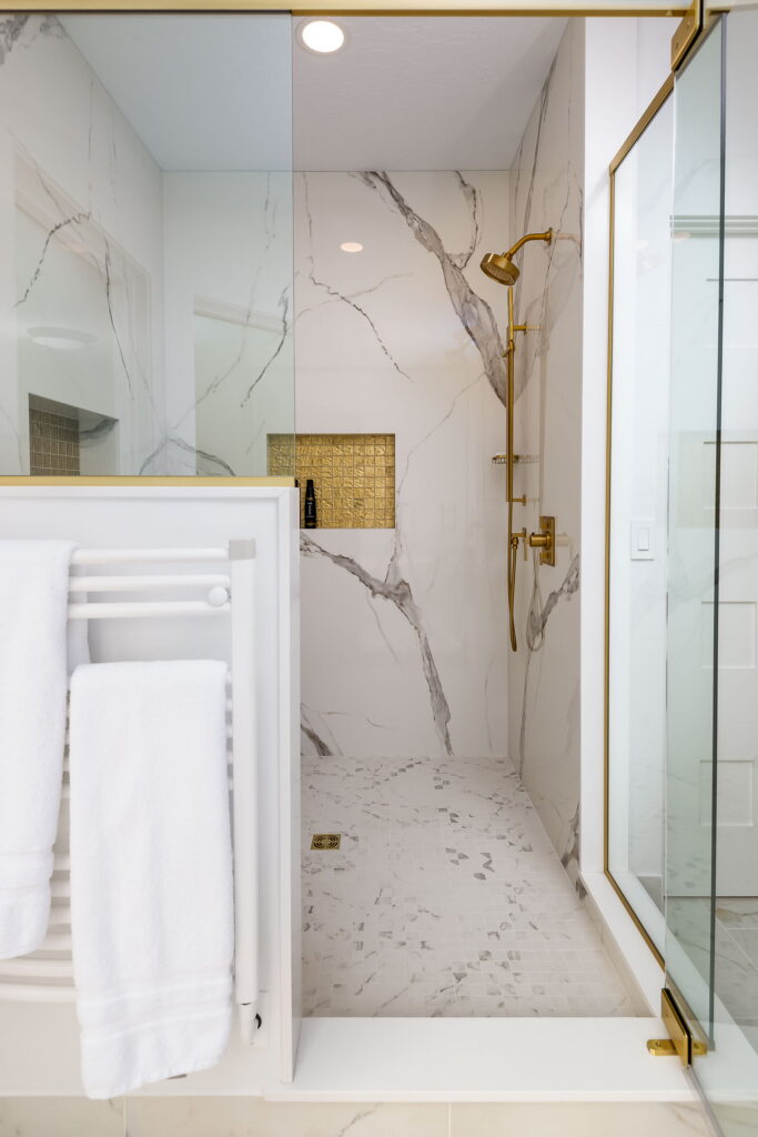 The tub and shower share the marble floor, with a towel warmer set between them.