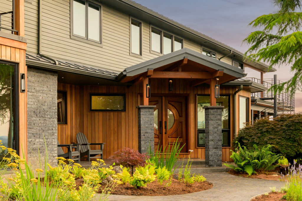 Craftsman home exterior remodel with cedar siding, stone columns, and round-window front door.