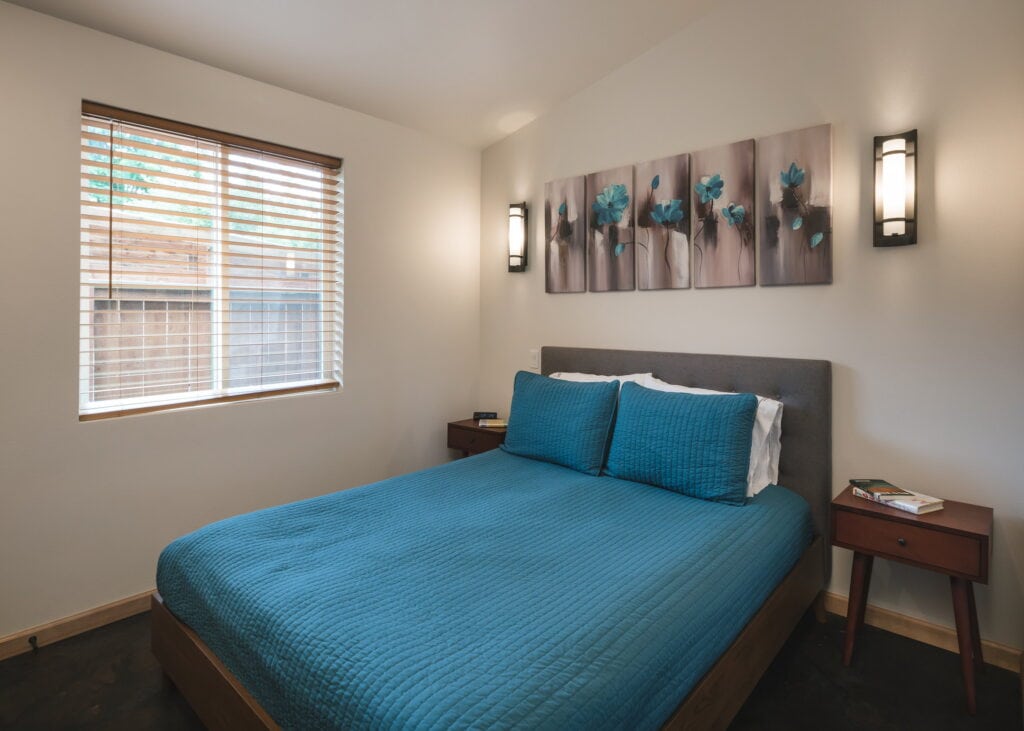 Bedroom with wall sconces, a wood-blind window, and stained concrete floors.