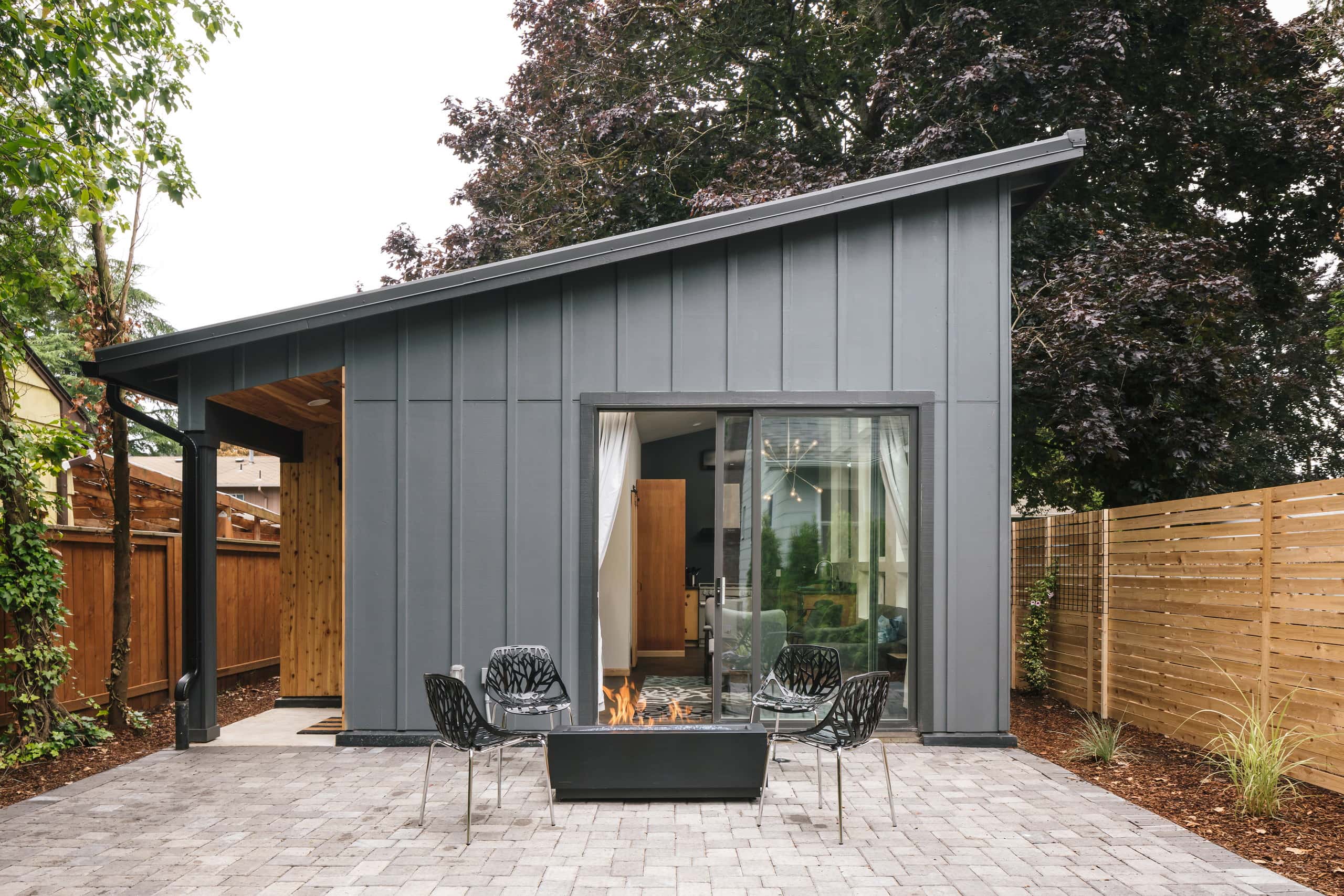 Modern Woodstock ADU with dark board-and-batten siding, a single-slope roof, and a paved patio with a gas fire table.