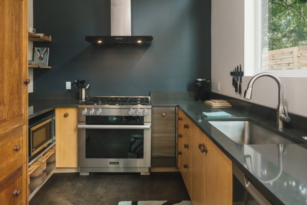 Stainless gas range and black hood on the painted accent wall, with dark quartz counters.