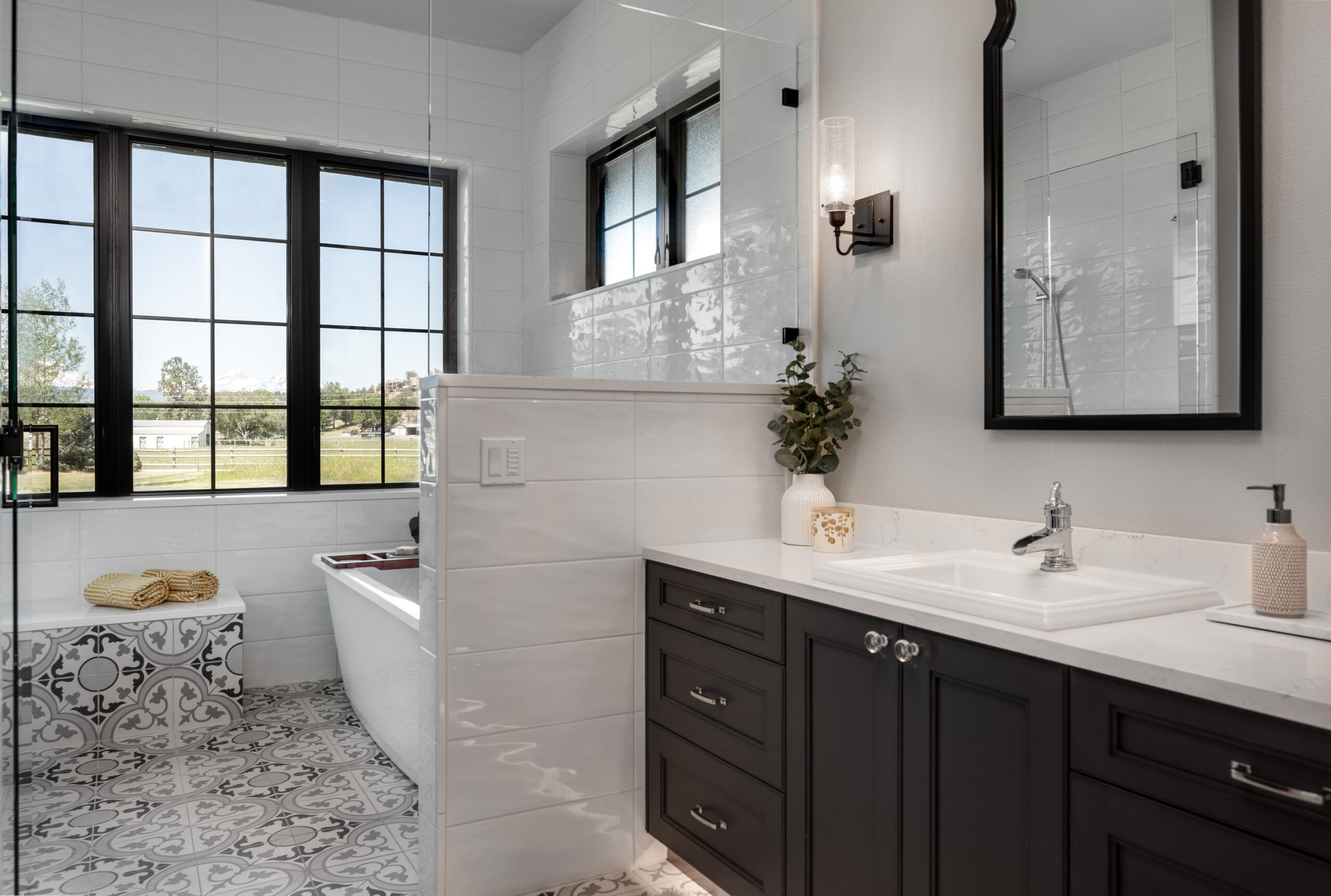 A remodeled bathroom with large windows, patterned tile floor, and charcoal cabinets