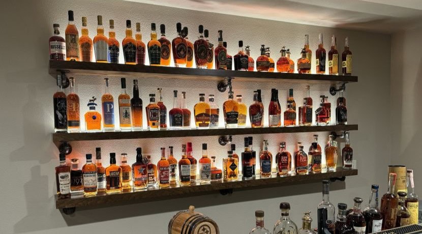 Three walnut bar shelves with steel brackets and up-lighting that makes liquor bottles glow