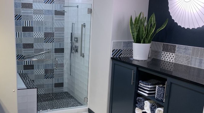 A walk-in shower with multi-patterned tile and polished nickel fixtures next to coordinating dark blue cabinets