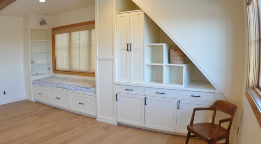 Custom-built white cabinetry installed under a sloped attic ceiling, plus a window seat