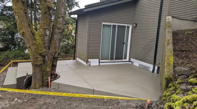 A new concrete patio poured around a tree and against a home with a sliding glass door and grey siding