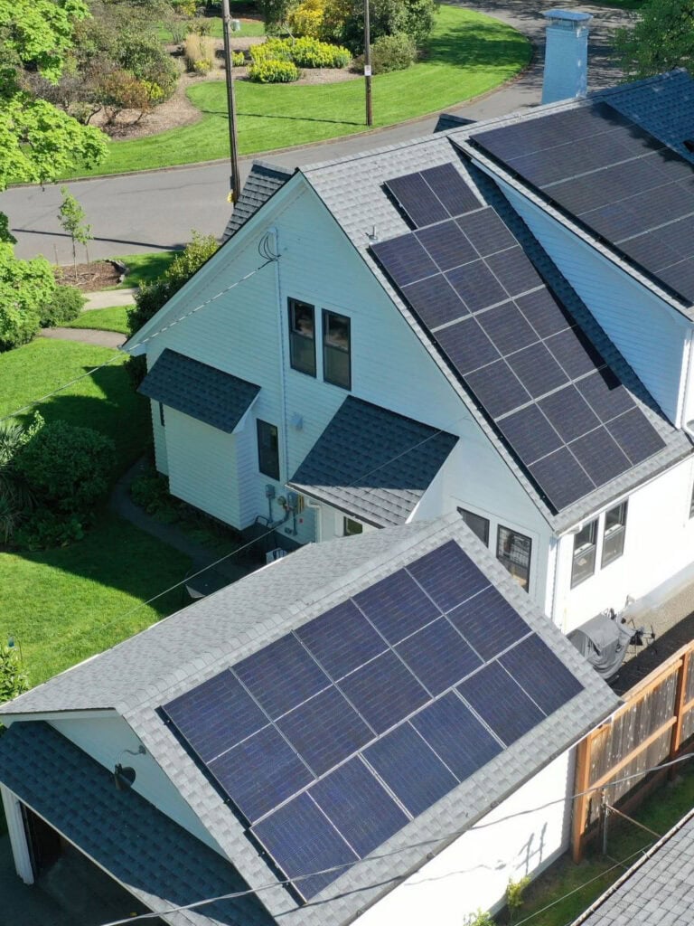 Aerial view of solar panels installed across the roof of a white Portland home and its detached garage.