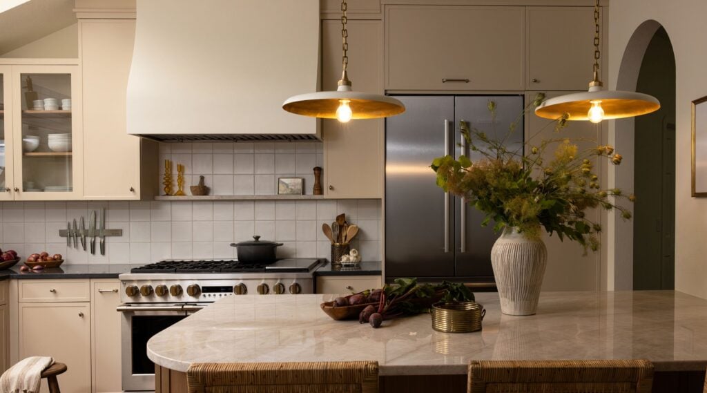 A remodeled kitchen with warm beige cabinets, two modern pendants over the island and a curved Taj Mahal Quartzite countertop