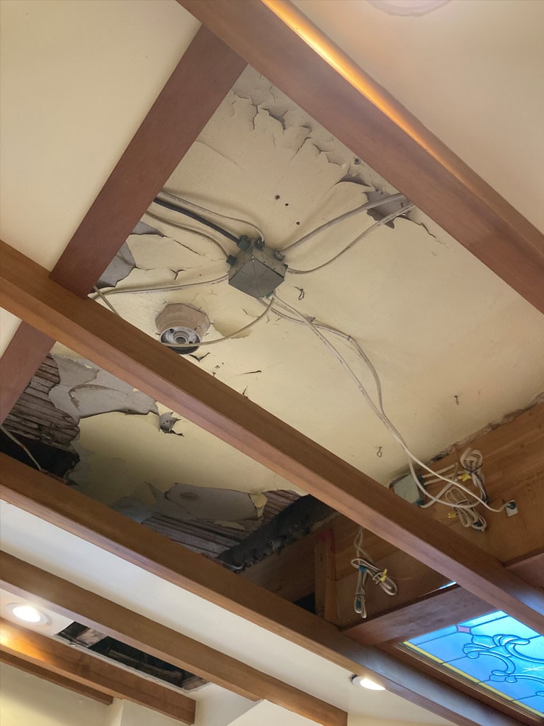 A ceiling with failing lath and plaster and exposed electrical wiring behind exposed beams