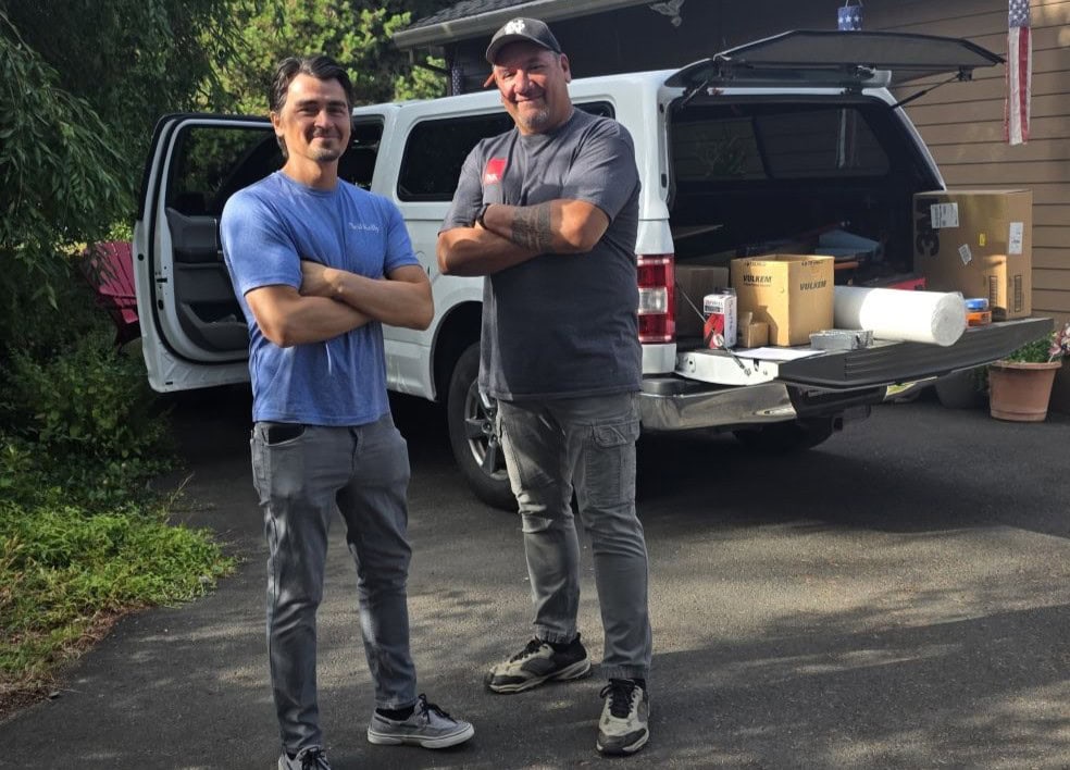 Two Neil Kelly carpenters standing next to each other confidently with arms crossed in front of a work truck