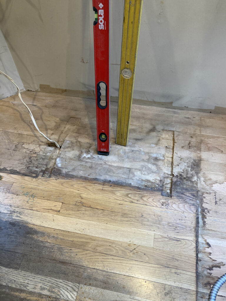 A hardwood floor with visible water damage and two levels leaning on the wall