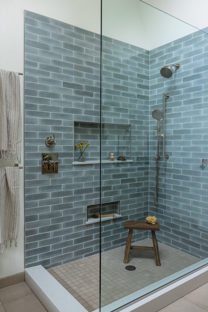 A remodeled shower with blue tile, a glass enclosure, and polished nickel fixtures