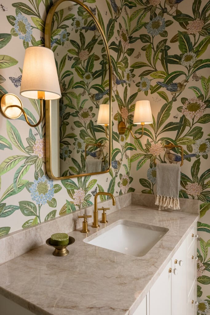 A remodeled bathroom with botanical wallpaper, lamp sconces, and taj mahal quartz countertop