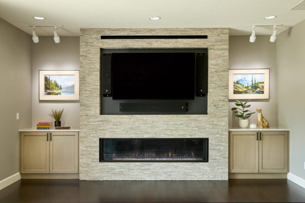 A ribbon-style fireplace with stone surround, a tv mounted above it, flanked by lower cabinet storage.