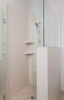 Bend Tetherow Custom Home 029 Modern Custom home bathroom shower with handmade tile, handheld shower head, shower shelf, and frameless shower surround.