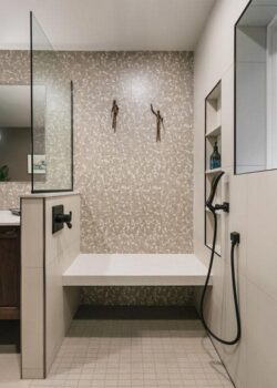 Tiled shower alcove with a black handheld shower head and quarts bench.
