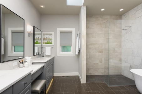 Two grey, cabinet vanities with a shelf in-between to the left of a glass, walk-in shower.