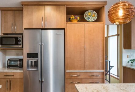 Stainless steel refrigerator with wooden refrigerator cabinets above and to the right for storage.