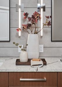 Two vases with flowers placed between two mirrors on top of a dual-sink vanity.