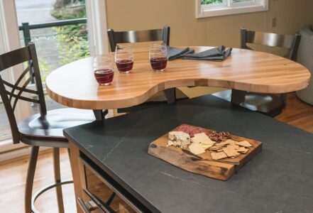 Three wine glasses on top of a wood finished hightop table with three dark stools.