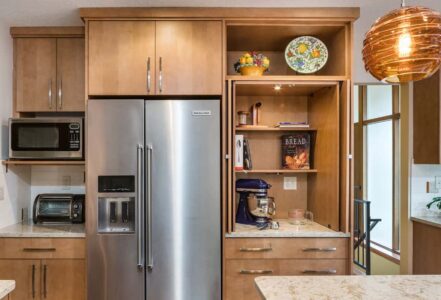 Stainless steel refrigerator with wooden appliance garage cabinets open to the right with a stand mixer and shelving.