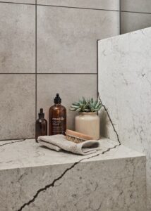 Two soap dispensers, a small potted plant, and folded towel on top of a shower bench with PentalQuartz tile.