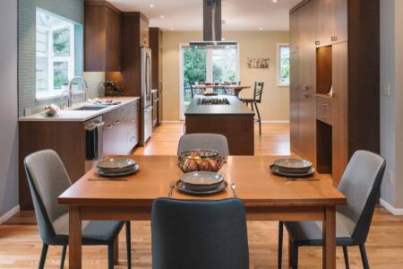 Wooden dining room table with four seating arrangements next to a living room space.