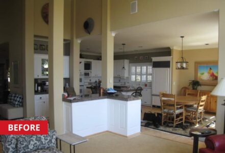 Kitchen with white, wood-paneled cabinetry, a center island, and a round wooden table with four seats below a hanging light.