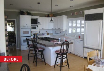 Kitchen with white, wood-paneled cabinetry, a center island, and a round wooden table with four seats below a hanging light.