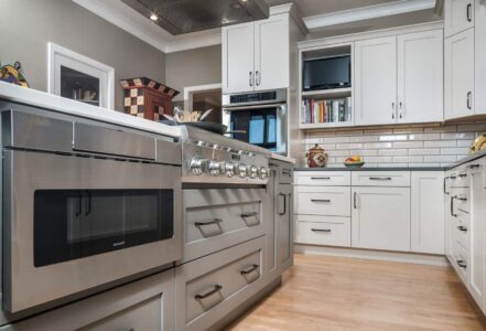 Stainless steel microwave to the left of shaker style cabinets built-in below a kitchen island.