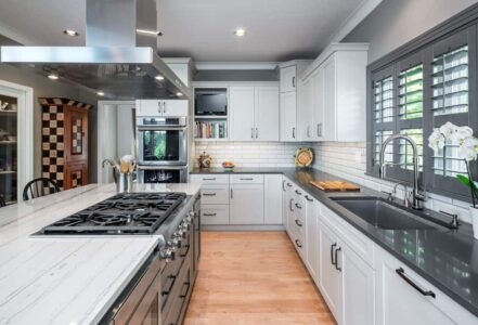 Modern kitchen with a quartzite island with a gas range, stainless steel air vent, and four black bar chairs.