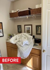 Kitchen countertop with wooden cabinets below, three paintings hanging on the wall, and a white metal shelf above.