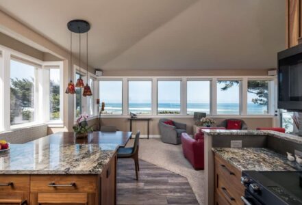 An open living room space with a dinner table below a hanging ceiling light, and two loveseats facing a hearth.