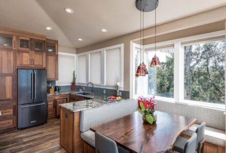 Kitchen table with banquette seating benches with grey cushions below three hanging lights.