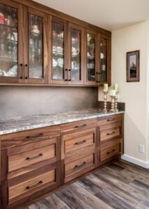 Walnut cabinets with glassware inside, above a granite countertop with walnut drawers below.
