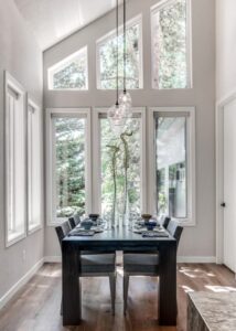 Black kitchen table with four grey chairs beneath two hanging lights with edison bulbs.