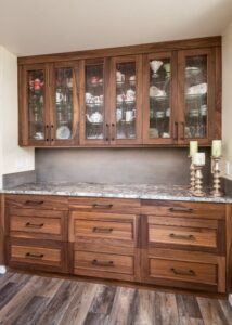 Walnut cabinets with glassware inside, above a granite countertop with walnut drawers below.