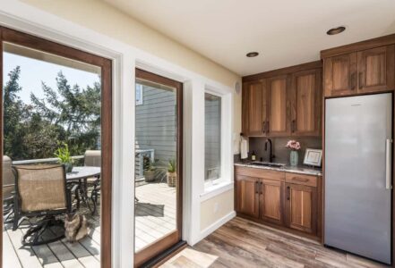 Large glass doors with walnut wood frames that lead out to an outside patio deck with a round table and four outdoor chairs.
