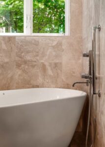 A white freestanding tub beneath a bathroom window.
