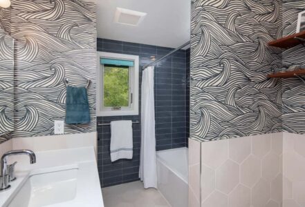 Bathroom shower tucked away behind a wall with a white shower curtain.